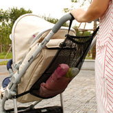 Baby stroller with a mesh organizer attached, containing a pink toy, with a blurred outdoor background.