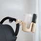 Beige cup holder attached to a stroller handle with a white cup and black phone inside.