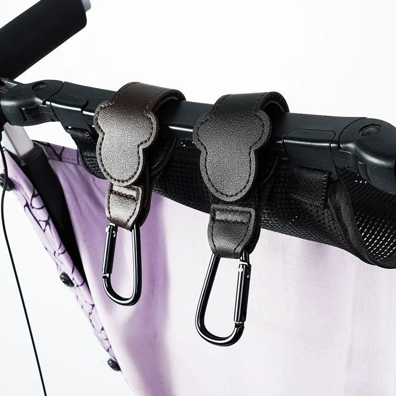 Black stroller hooks attached to a stroller with a white background