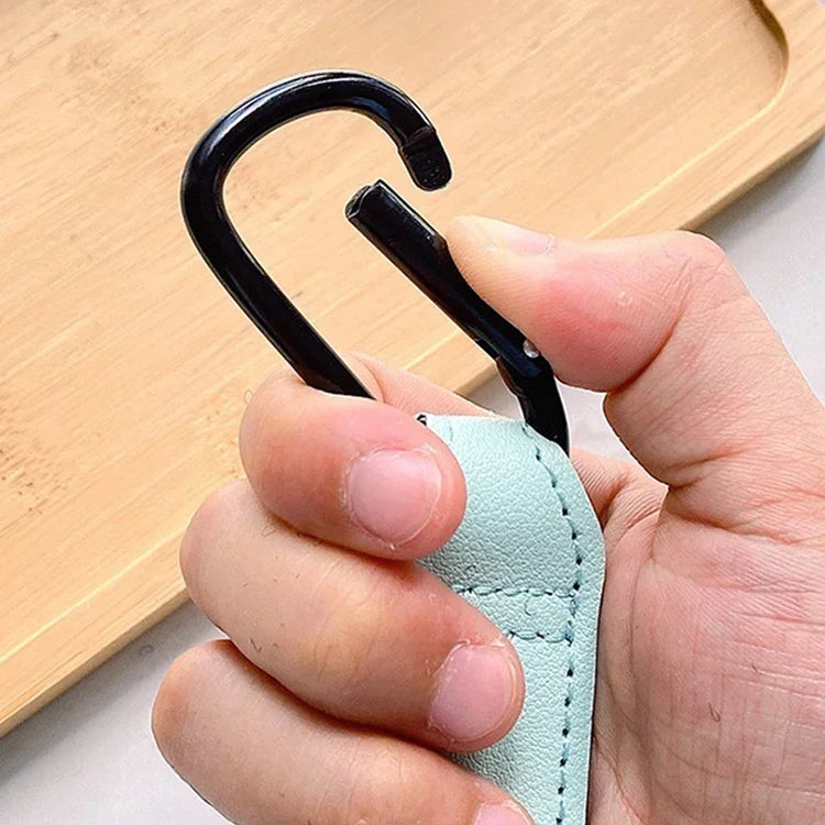 Hand holding a black carabiner attached to a light blue strap against a wooden background