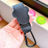 Black carabiner held in a hand with colorful objects in the background