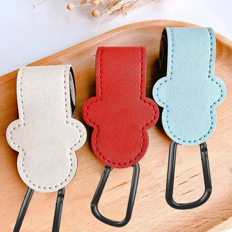 Three leather keychains in white, red, and light blue on a wooden surface.
