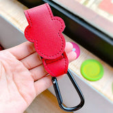 Red leather keychain with carabiner held in a hand, with colorful objects in the background.