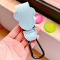 Light blue keychain with carabiner held in a hand, with colorful objects in the background.